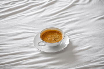 White cup with americano coffee stand on the bed with white sheet