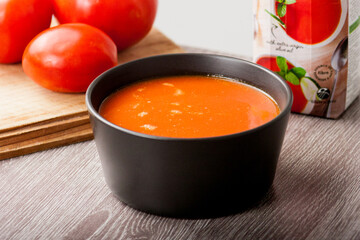 Tomato soup served in a black bowl with fresh tomatoes