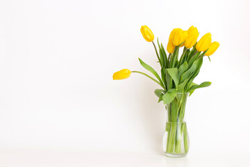 An exquisite bouquet of yellow tulips in a glass vase on a white background.