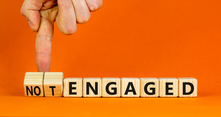 Engaged or not symbol. Concept words Engaged and Not engaged on wooden cubes. Businessman hand. Beautiful orange table orange background. Business engaged or not engaged concept. Copy space.