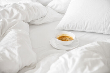 White cup of americano coffee stand on bed with white sheet, blanket and pillows