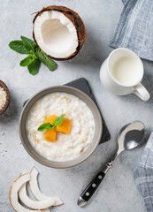 Rice porridge with coconut milk and mango slices in bowl on a blue background. Concept of a nutritious and satisfying food.