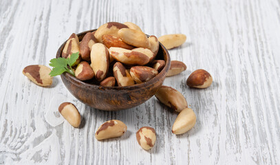 Brazil nuts raw and peeled in a wooden cup on a white wooden background. Rustic style. The concept of vegetarian and diet snacks.