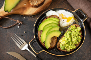 Wholemeal bread toast sliced avocado and poached egg on a stone background. Healthy breakfast concept, sandwich with avocado and egg.