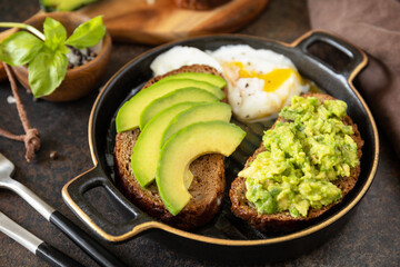 Healthy breakfast concept, sandwich with avocado and egg. Wholemeal bread toast sliced avocado and poached egg on a stone background.