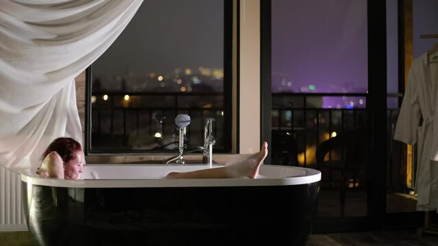 Girl Lies In A Bathtub With Panoramic Windows At Night, City Lights