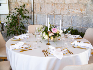 Wedding banquet concept. Chairs and round table for guests, served with cutler and, flowers and crockery and covered with a tablecloth