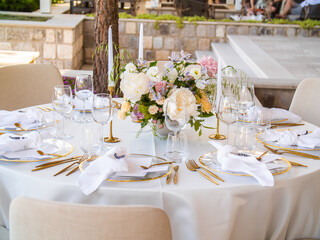 Beautiful outdoor wedding decoration in city. Candles and dried flowers and accessories with bouquets and glasses on table with linen tablecloth on newlywed table on green lawn