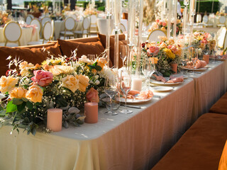 Beautiful outdoor wedding decoration in city. Candles and dried flowers and accessories with bouquets and glasses on table with linen tablecloth on newlywed table on green lawn