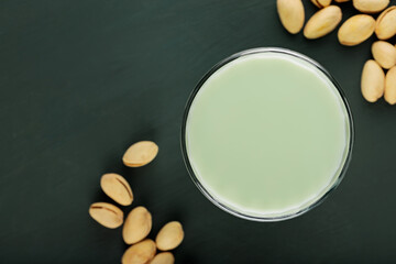 Pistachio milk in a glass on a dark green background. Healthy lactose-free pistachio milk and pistachios. Vegan nutty plant based milk. Top view. Copy space