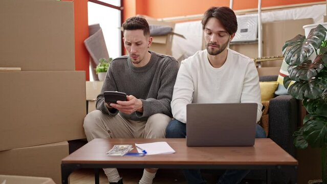 Two men couple using laptop counting dollars at new home