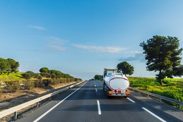 Fuel tanker truck driving on the highway with a nice countryside landscape in the background.