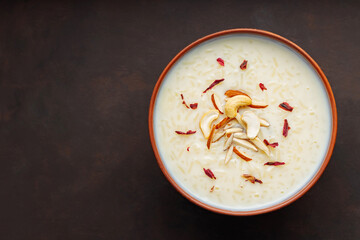 Bowl with rice pudding on dark background. Creamy rice kheer with cashew nuts and almonds. Copy...