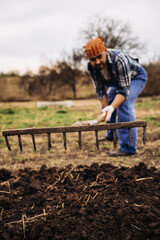 Farmer working in the garden with the help of a rake leveling plowed land, on a sunny day