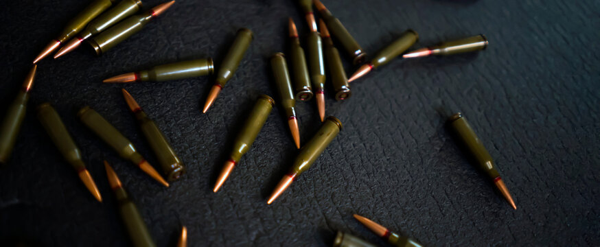 Scattered on a dark surface are bullets, cartridges for a kalashnikov assault rifle.