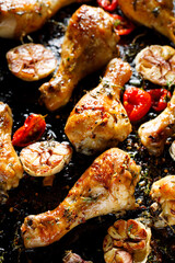 Spicy roasted chicken legs, drumsticks seasoned with garlic, hot peppers and aromatic herbs on a black background, close-up