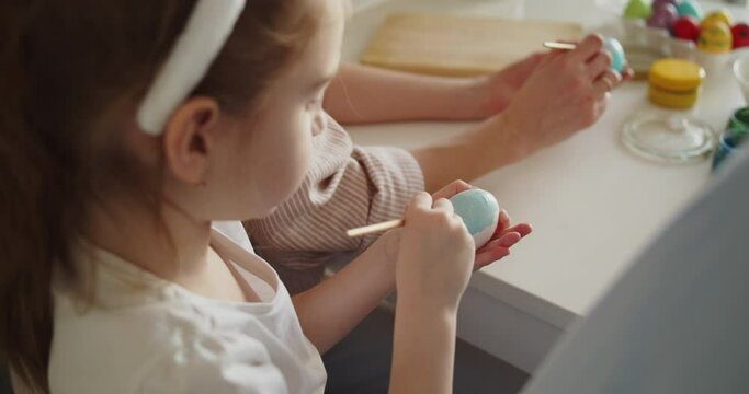 Young girl painting Easter egg sitting at the table in bright modern kitchen. Preparation for Easter. Close-up shot.