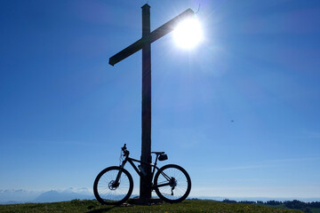mountain bike on summit cross against blue sky and sun