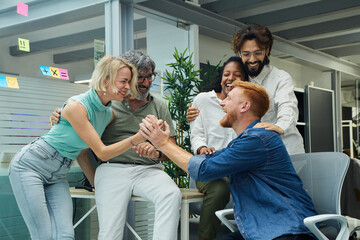 Portrait of a very excited multiracial work team celebrating a new professional success, young and mature colleagues with laughing expression. Group of office workers in a start-up company.