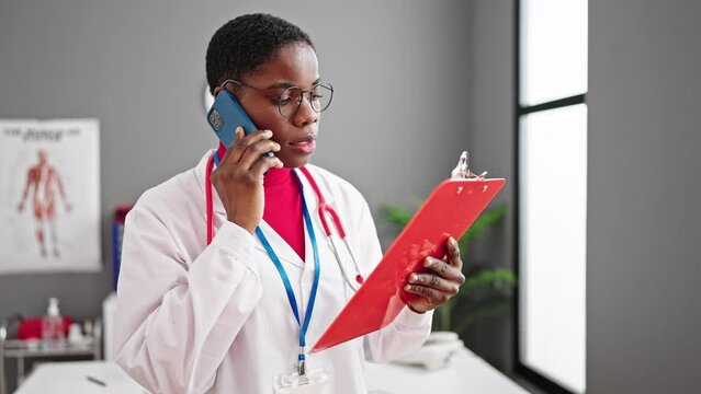 African american woman doctor talking on smartphone reading document at clinic