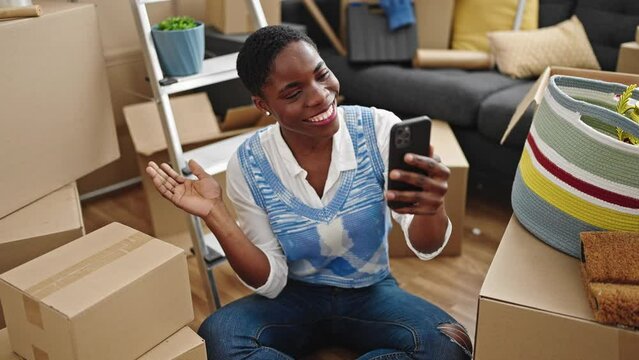 African american woman having video call sitting on floor at new home