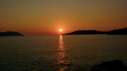 Fiery red sunset over sea between mountains in sea or ocean. Picturesque sunrise with sunny path on water. concept of end of career or its beginning. Natural phenomenon in morning.