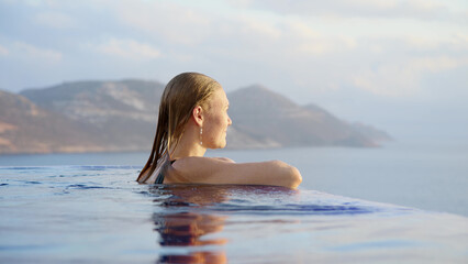 young woman at midday in infinity pool on edge of abyss. girl looks into distance, concept of loneliness and happiness to be alone for peace and tranquility.