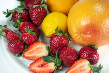 Fototapeta na wymiar White Plate of fruits strawberry and grapefruit, lemon and orange