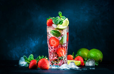 Strawberry Mojito cocktail drink with lime, white rum, soda, cane sugar, mint, and ice in glass on deep blue background. Summer refreshing beverage