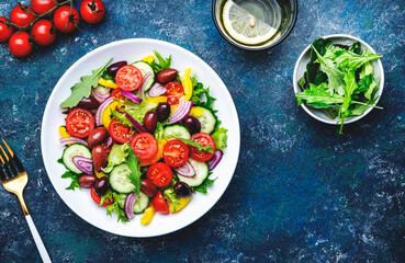 Vegan greek salad with kalamata olives, red tomato, yellow paprika, cucumber and onion, healthy mediterranean diet food, low calories eating. Blue stone background, top view