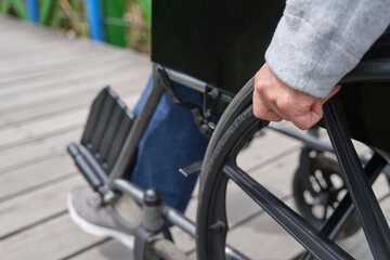 Obraz premium Unrecognizable woman strolling in a wheelchair, outdoors. Close up of a female hand moving the wheelchair forward.