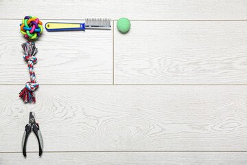 Grooming comb, nail clipper and toys on light wooden background