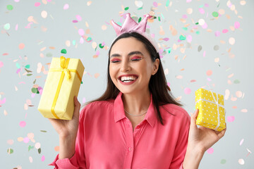 Happy young woman with Birthday gifts on grey background