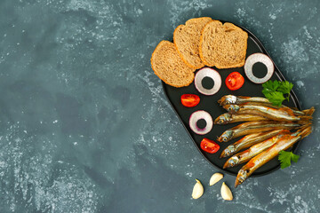Board with delicious smoked capelin, bread pieces and vegetables on grey grunge background