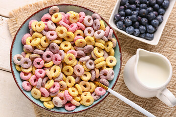 Bowl of colorful cereal rings, pitcher with milk and blueberries on white wooden background