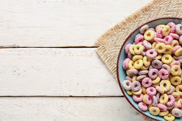 Bowl of colorful cereal rings on white wooden background