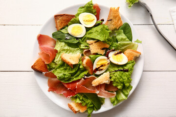 Plate of delicious salad with boiled eggs and jamon on white wooden background