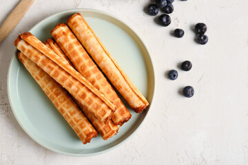 Plate of wafer rolls with boiled condensed milk and blueberries on white grunge background
