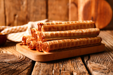 Board of wafer rolls with boiled condensed milk on brown wooden table, closeup