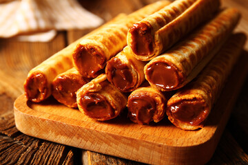 Board of wafer rolls with boiled condensed milk on brown wooden table, closeup
