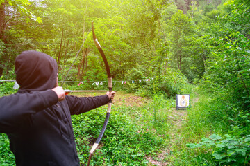 Young archer aiming arrow at target board. Man with bow and arrow aiming at archery target in...