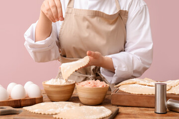 Woman preparing tasty meat empanadas at wooden table near color wall