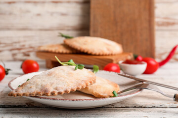 Plate with baked meat empanadas on light wooden table, closeup