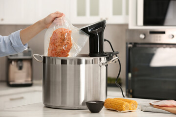 Woman putting vacuum packed meat into pot with sous vide cooker in kitchen, closeup. Thermal...