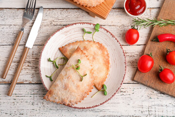 Plate with baked meat empanadas, sauce and vegetables on light wooden background