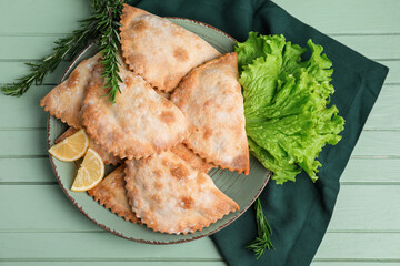 Plate with baked meat empanadas, lettuce and rosemary on color wooden background