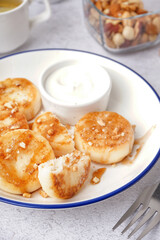 Plate of tasty cottage cheese pancakes with sour cream on light background, closeup