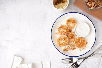 Plate with tasty cottage cheese pancakes, sour cream and cup of tea on light background