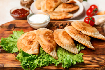 Wooden board with tasty meat empanadas, lettuce and sauces, closeup
