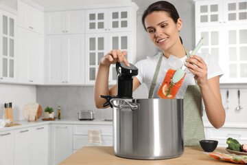 Woman putting vacuum packed salmon into pot and using thermal immersion circulator at table in...